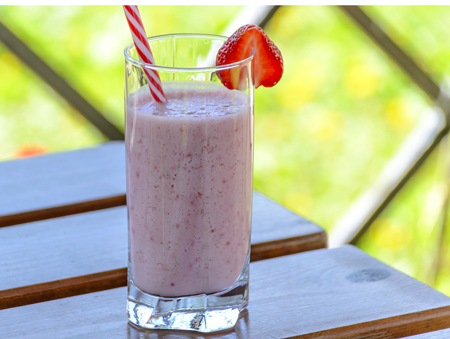 Strawberry kefir in a tall glass adorned with a strawberry slice and a bright red straw.