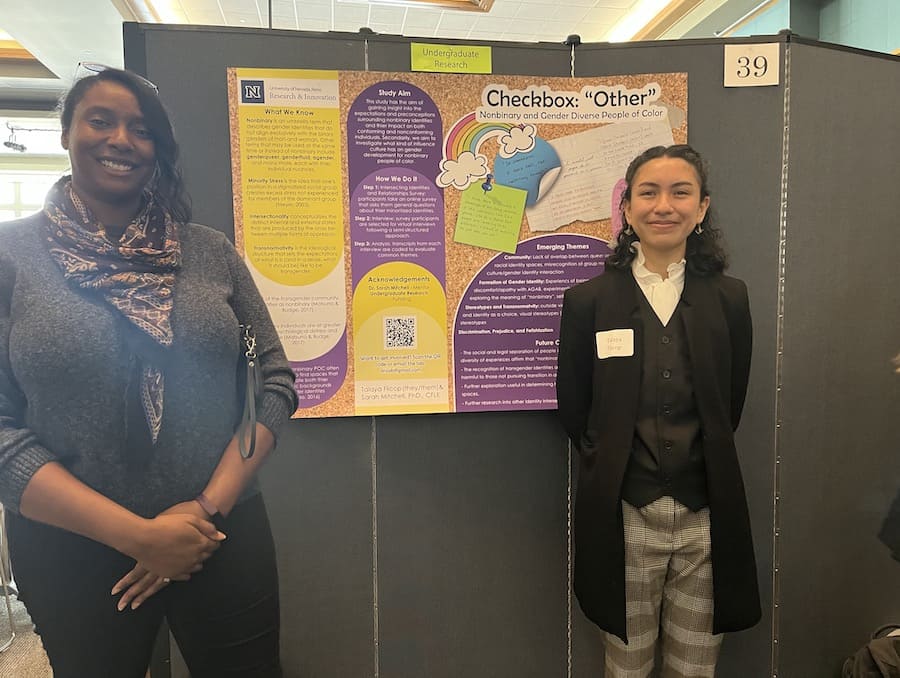 Dr. Sarah Mitchell and her mentee Talaya Flicop posing with Flicop's final version of their Undergraduate Research project.