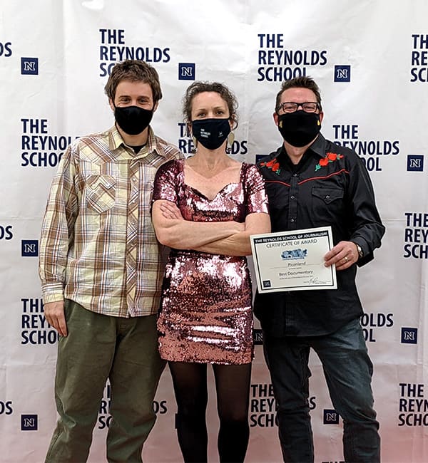 Richard Bednarski, Kari Barber and Mark Maynard stand in front of a white background that says "Reynolds School of Journalism."