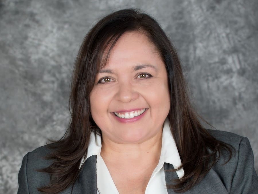 Woman smiling for headshot photo in front of a grey background.