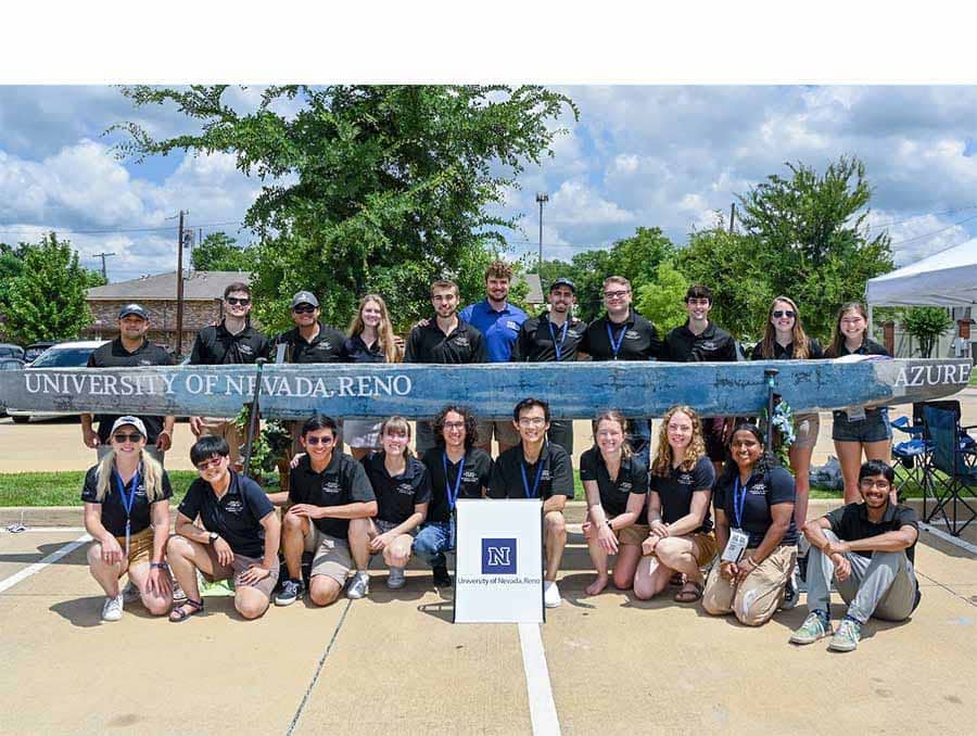 Twenty-one people standing and kneeling around a canoe outdoors