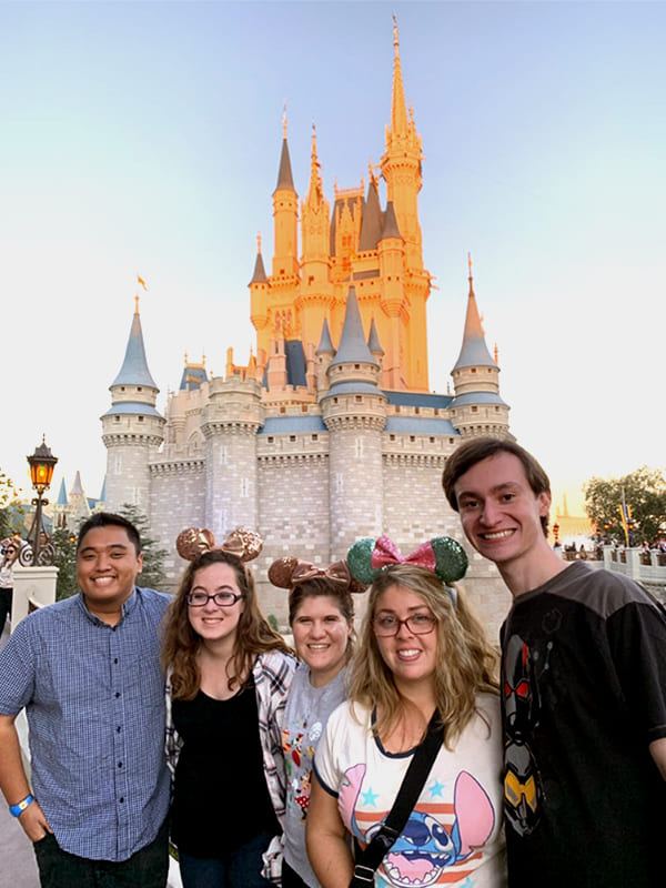 A group of friends stand together and smile to the camera with the Disneyland Sleeping Beauty Castle behind them.