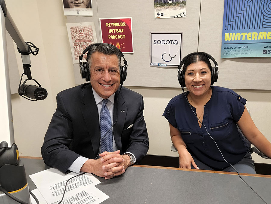 President Brian Sandoval and Markie Wilder smile while sitting next to each other, wearing headphones in the recording space