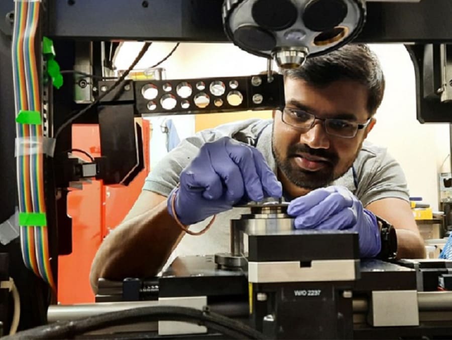 Ashish Kasar leaning forward in frame, with gloved hands, working on equipment.