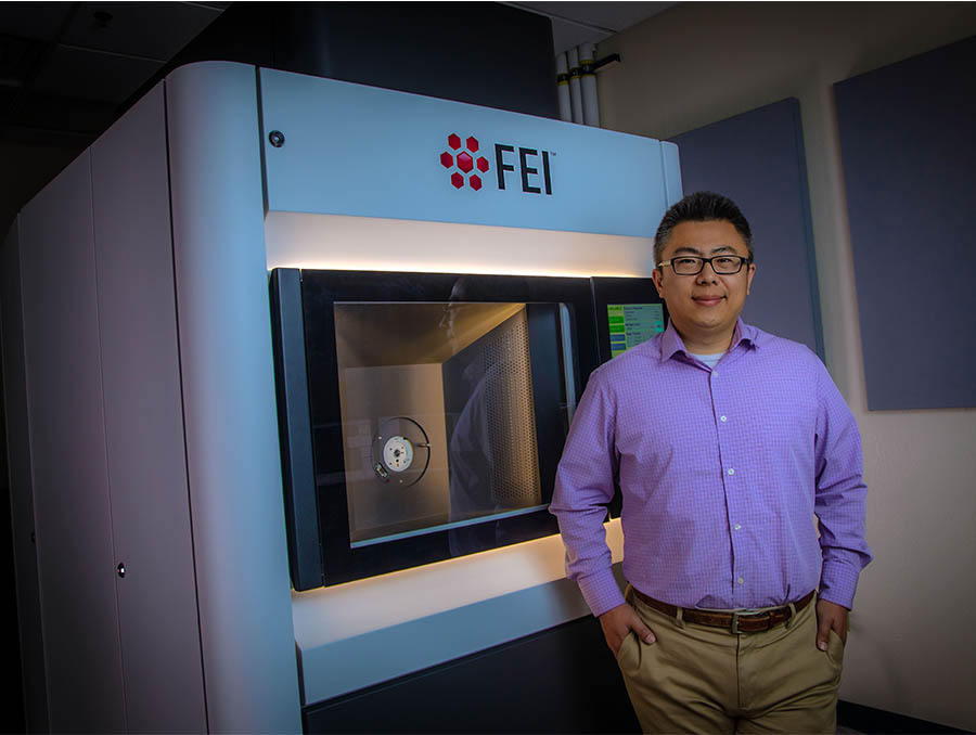 Chemical & Materials Engineering Assistant Professor Yufeng Zheng stands in front of an electron microscope.