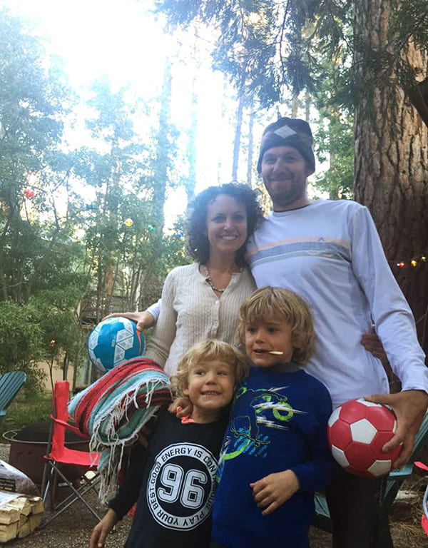 Kari Barber and Nico Colombant pose with two of their sons in front of a forest background.