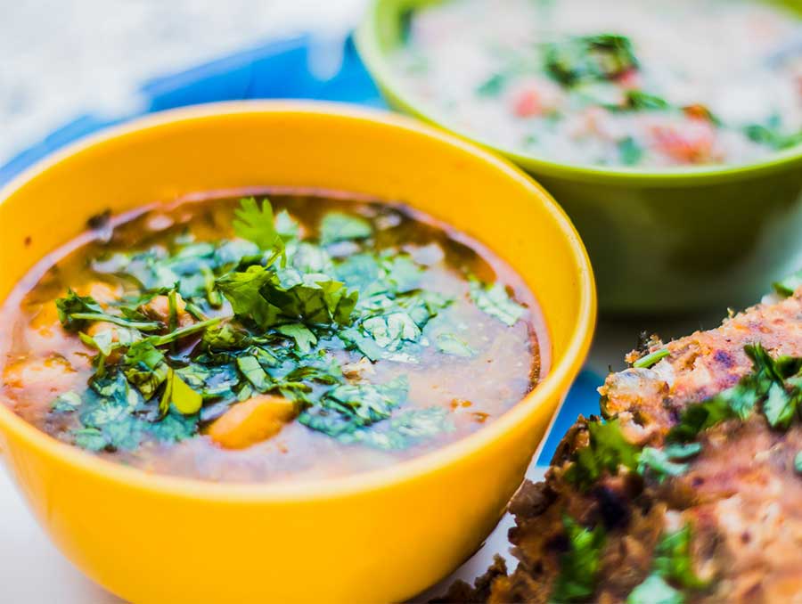 Curry in a bright yellow bowl, alongside other Indian dishes in bright green and blue containers.