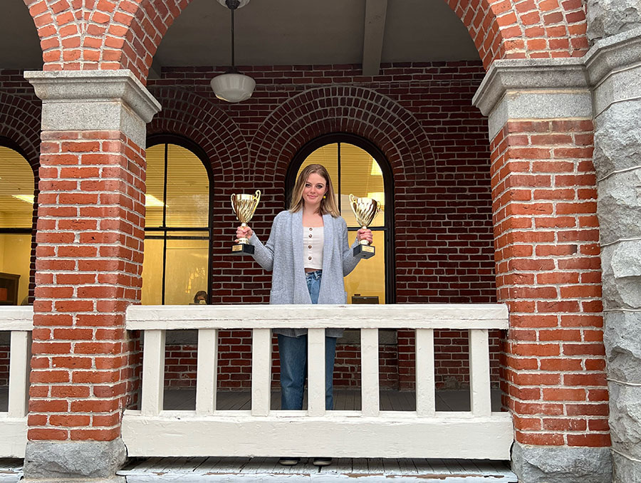 Hannah Branch stands on porch holding two trophies up