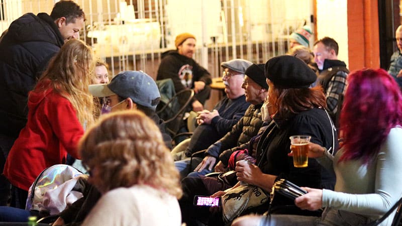 A group of people, dressed warmly in coats and hats, sitting in chairs and chatting among themselves. 