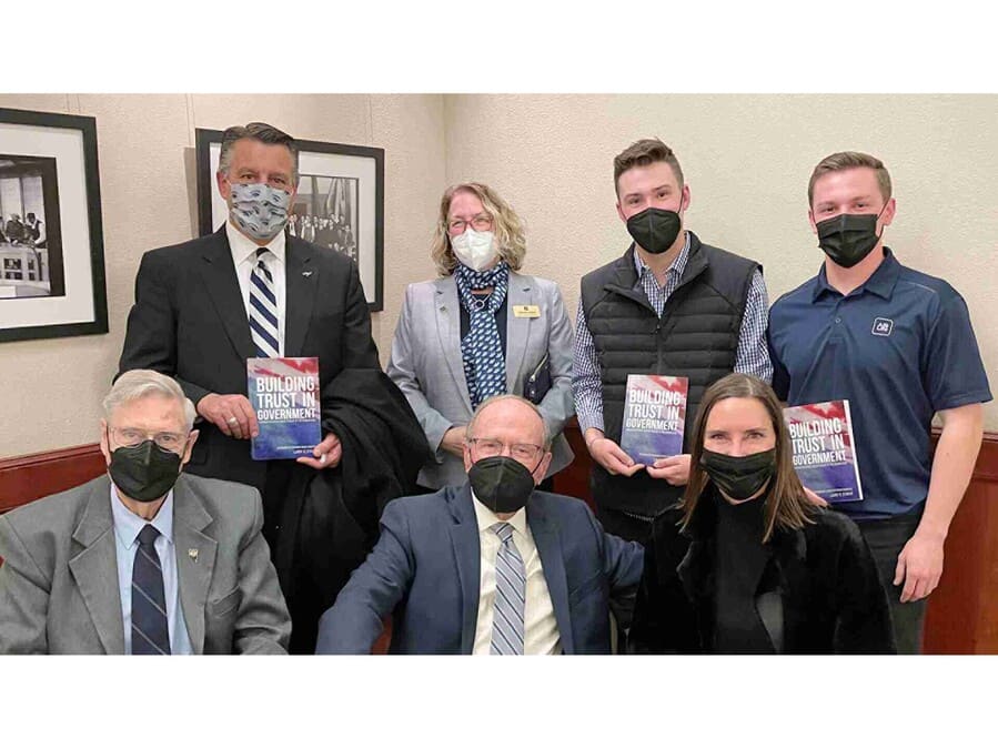 Seven people seated and standing with some holding copies of Larry Struve’s new book “Building Trust in Government.”