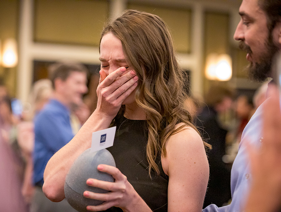 A student holds a large egg which contains her residency match while covering her mouth.