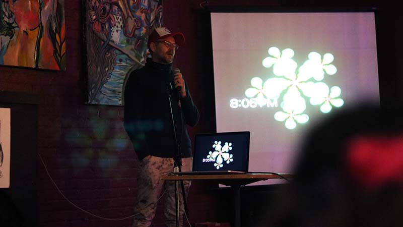 Nico Colombant stands in front of a screen while speaking into a microphone.