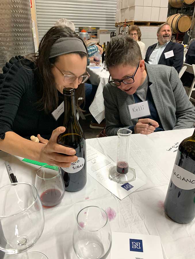 Two people blending red wines in a graduated cylinder.