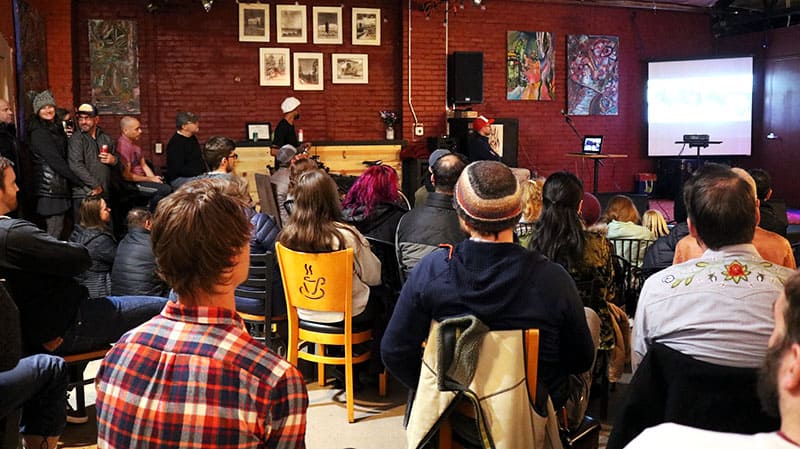 A group of people sitting in chairs look toward a screen in the corner of the room.