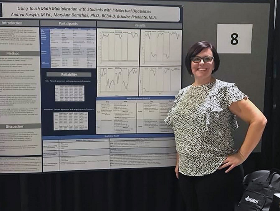 Jodee Prudente stands in front of a presentation board about a project working with students with disabilities