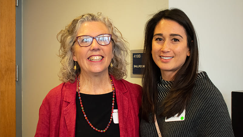 A close-up of two women standing together and smiling to camera.