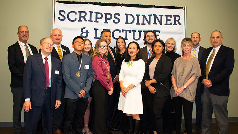 University of Nevada, Reno President and First Lady Sandoval stand next to the 2022 Scripps Scholarship and Internship recipients, Scripps family and foundation members, Reynolds School of Journalism Dean Alan Stavitsky and Kristen Go in front of a banner that says "Scripps Dinner and Lecture."