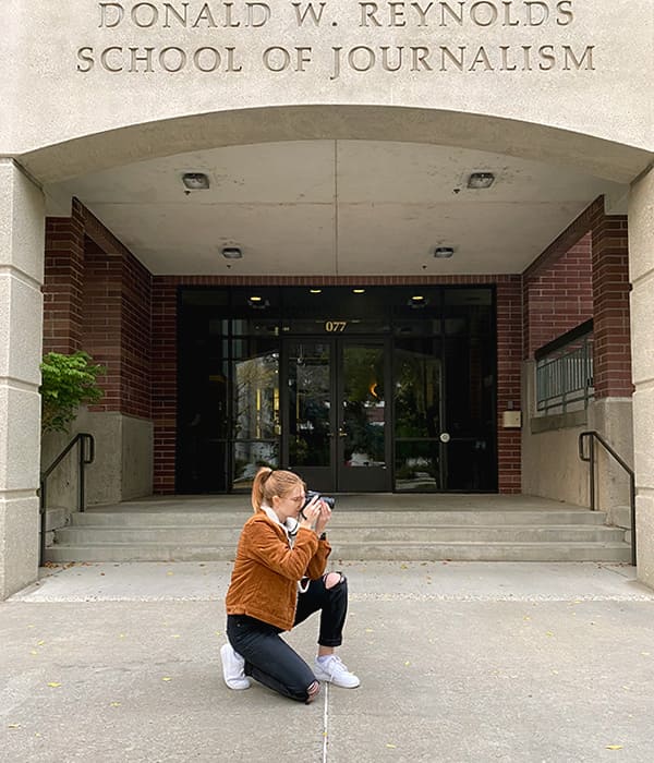 Alina Croft taking a picture in front of the Reynolds School of Journalism building.