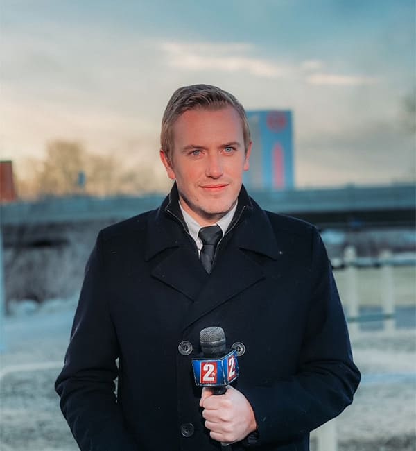 Bryan Hofmann stands in front of a blue sky background while holding a KTVN microphone.
