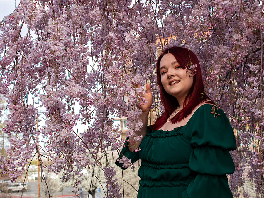 Catherine Schofield stands in front of pink flowers and smiles to camera.