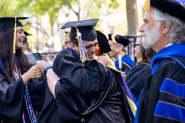 A graduate hugs a professor emotionally with a diploma in hand
