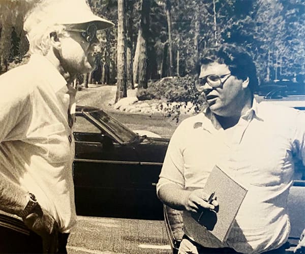 A black and white photo of Guy Clifton interviewing  a man and while holding a notebook and a pen.