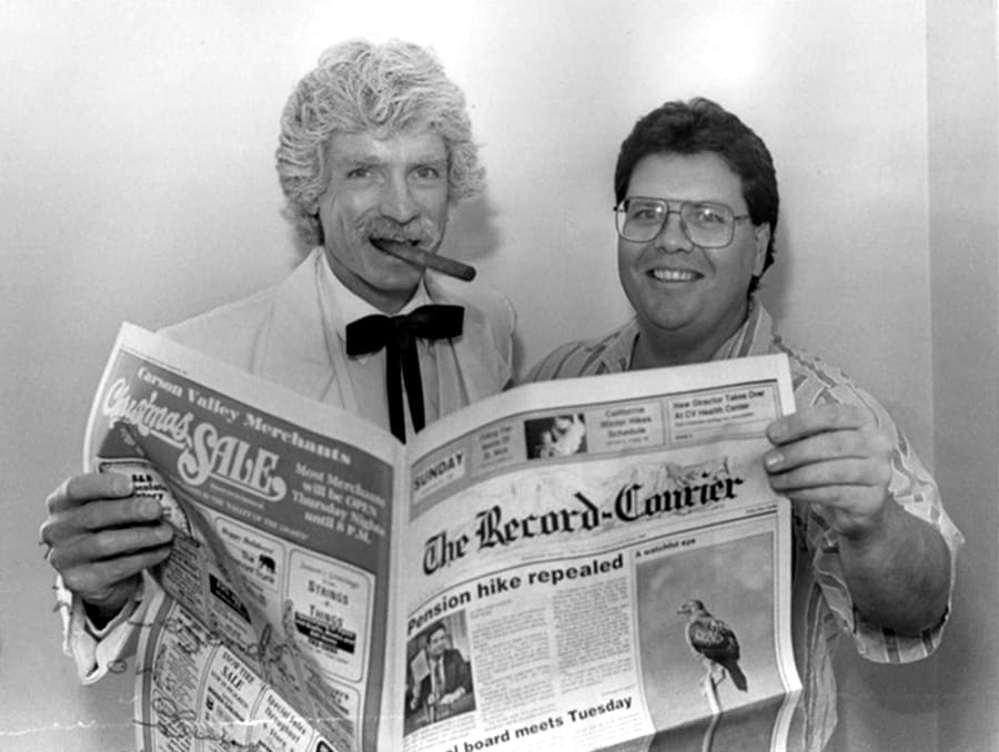 A black and white photo of Guy Clifton holding up a newspaper with a Mark Twain impersonator. 