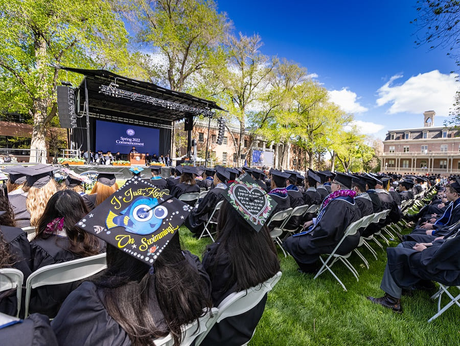 The Quad packed full of graduates looking at the stage. A mortar board in the foreground reads, "I just kept swimming."