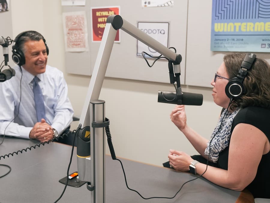President Brian Sandoval and Professor Sarah Cummings talk into microphones and wear headphones in the recording space