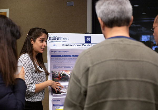A woman stands by a poster explaining an experiment, three people look on.