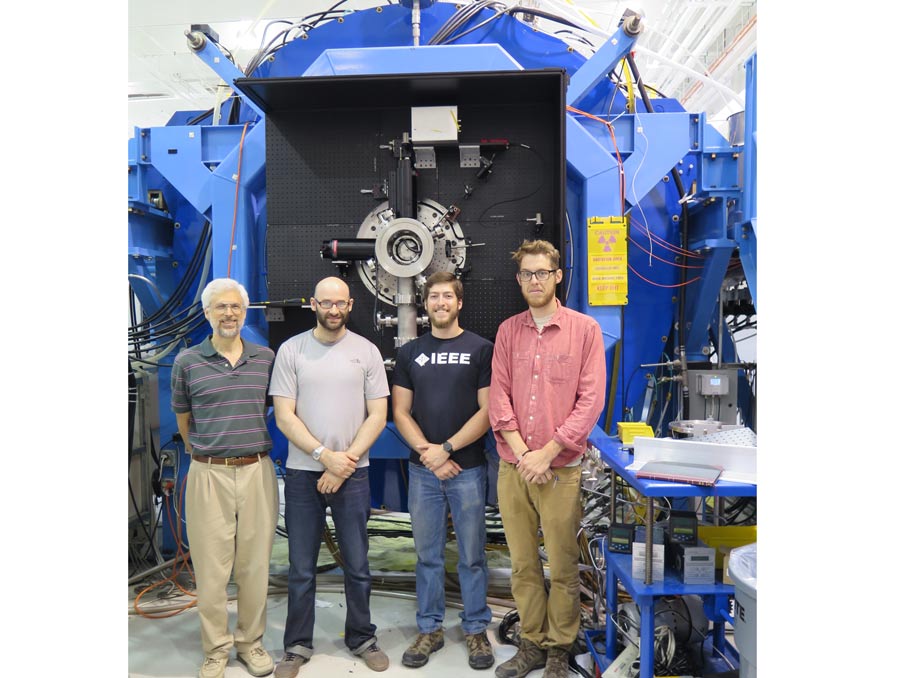 Four men stand in front of a large blue machine.