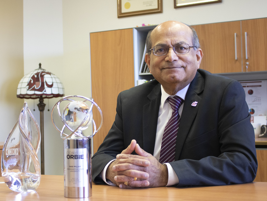 Dr. Sasi Pillay sits at a desk in a suit next to awards for CIO and ORBiE.