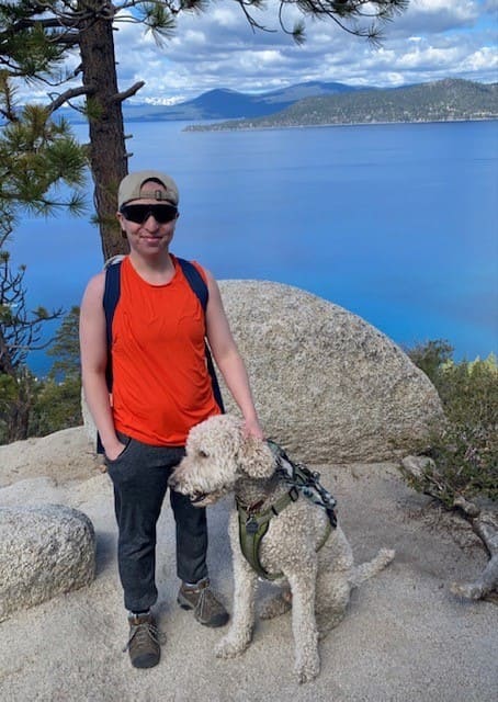 Owner and their dog on a trail with a lake in the background.