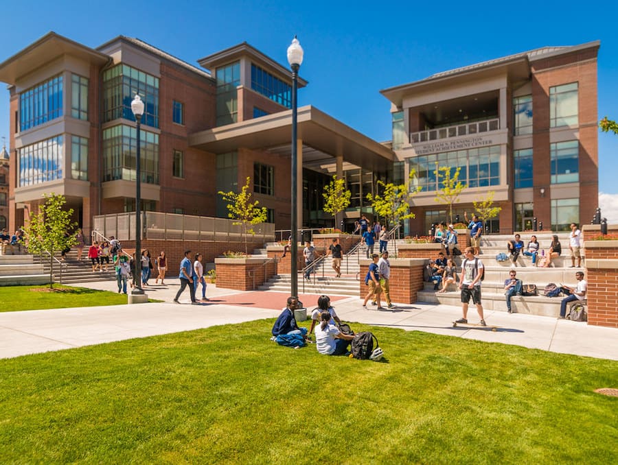 The front of the Pennington Student Achievement Center with two students sitting in the grass and several students walking behind them. 