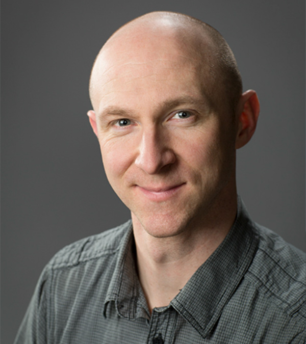 Portrait of Daniel Fergus wearing dark, short-sleeve collared shirt.