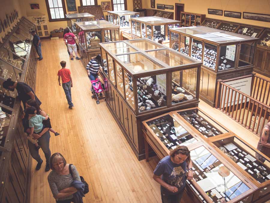 People walk around the wooden and glass cases holding rock specimens in the Keck Museum. The photo is taken from above.