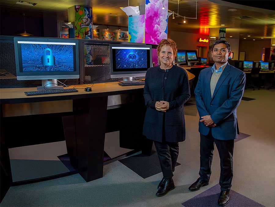 Professor LaTourette and Professor Sengupta, in professional attire, stand next to computers in a computer lab.
