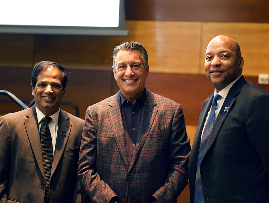 Three men in suits standing in a row in a conference room.