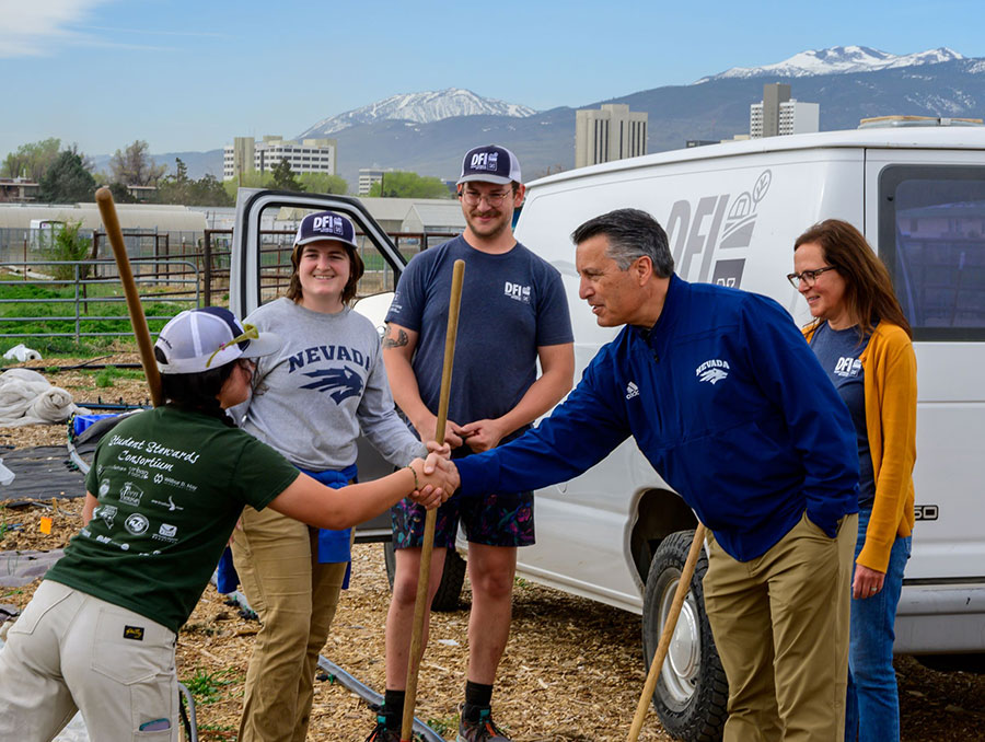 President Sandoval shaking a student's hand on a farm.