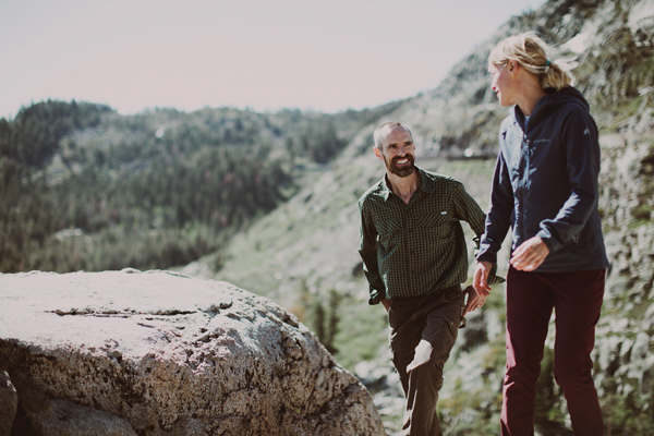 A man and a woman walk toward the camera. The woman is looking away, toward the man. They are both smiling.