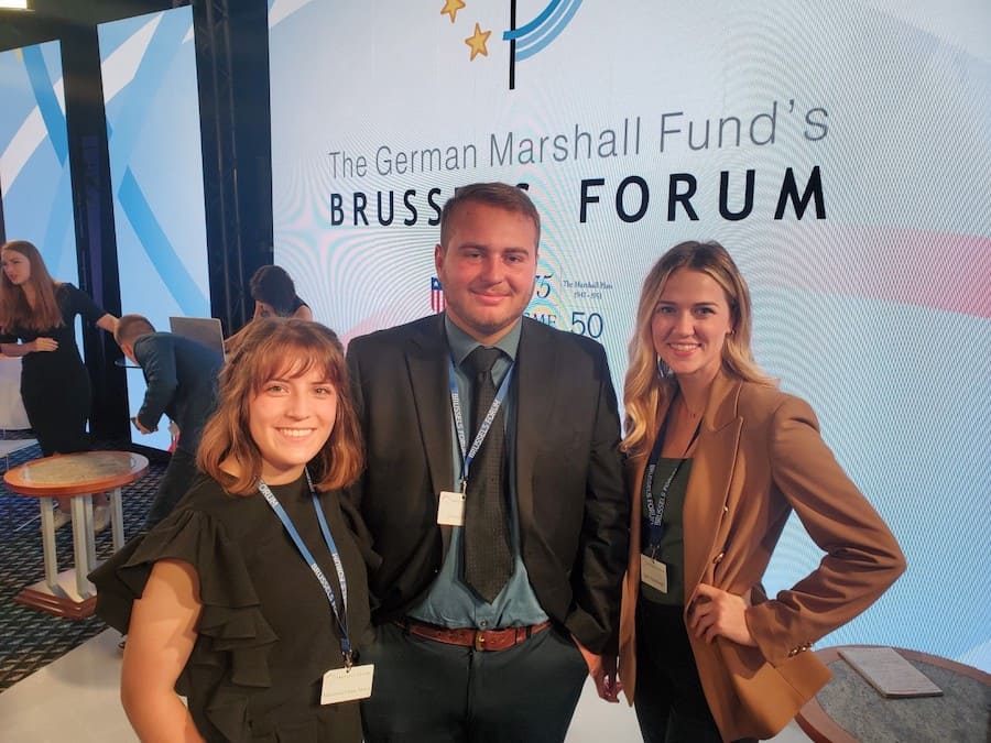 Three students (two girls and one boy) at a forum in professional attire.