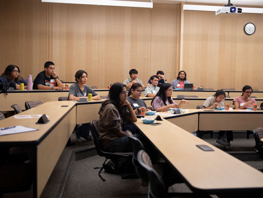 Students sit in a classroom. Some of them are eating nachos.