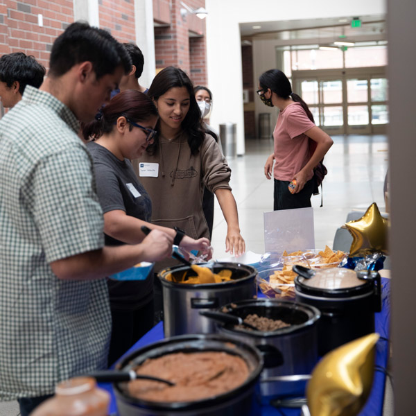 Students line up along a table with various toppings for nachos.