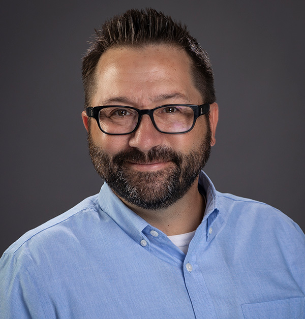 Portrait of Martin wearing dark-framed glasses and a light blue collared shirt.