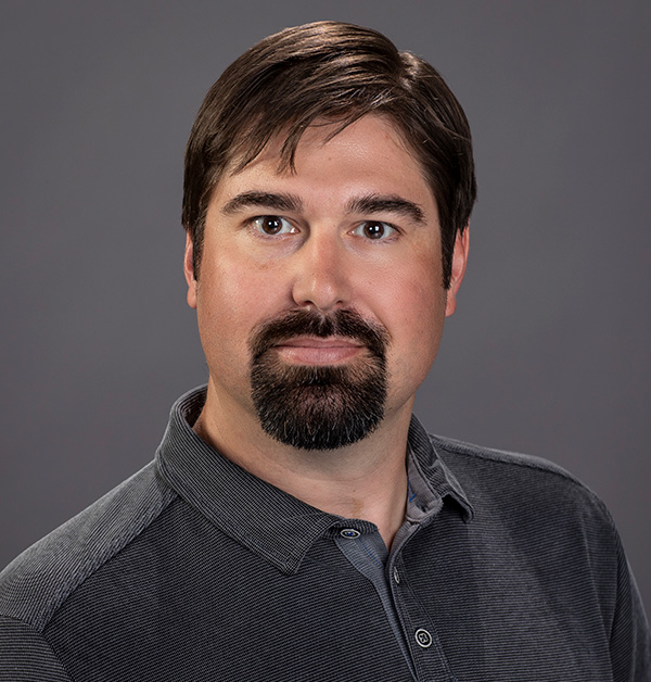 Portrait of Nick wearing a black collared shirt.