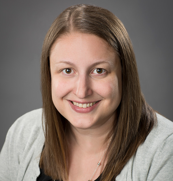 Portrait of Teresa Schultz wearing a light grey cardigan with a long, beaded necklace and a dark camisole.