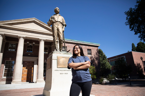 A woman wearing a blue t-shirt smiles and looks upward next to the Mackay statue.