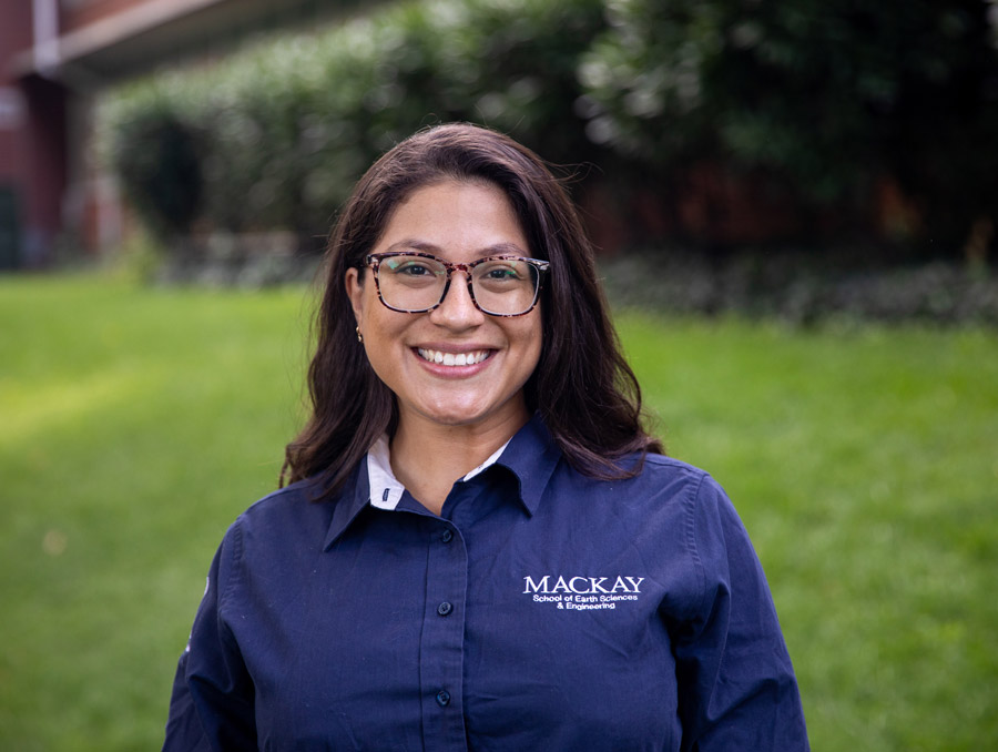 Isabel Peñaloza Araujo poses for the camera. She has dark hair, wears glasses and a blue Mackay polo, smiling.