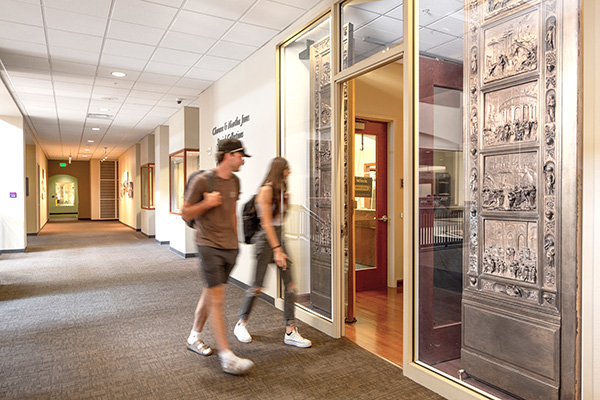 A male student carrying a backpack walks along-side a female student in black jeans and a sleeveless shirt. Both are entering Special Collections and University Archives located on the third floor of the Mathewson-IGT Knowledge Center.