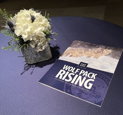 White roses in a vase on a table. Next to the vase is a copy of the new University Strategic Plan, Wolf Pack Rising.